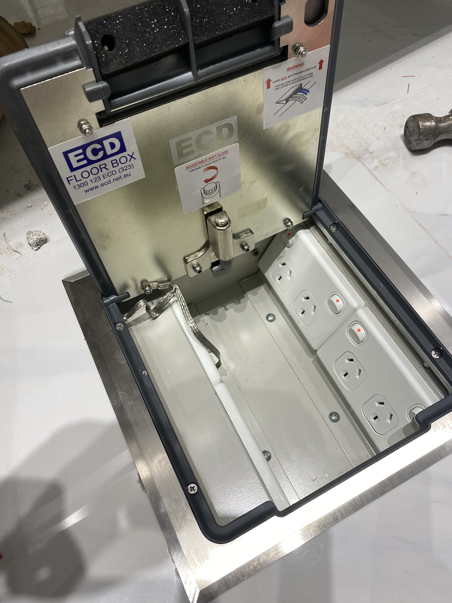 Recessed stainless steel floor power box with dual outlets flush-mounted into tiled flooring