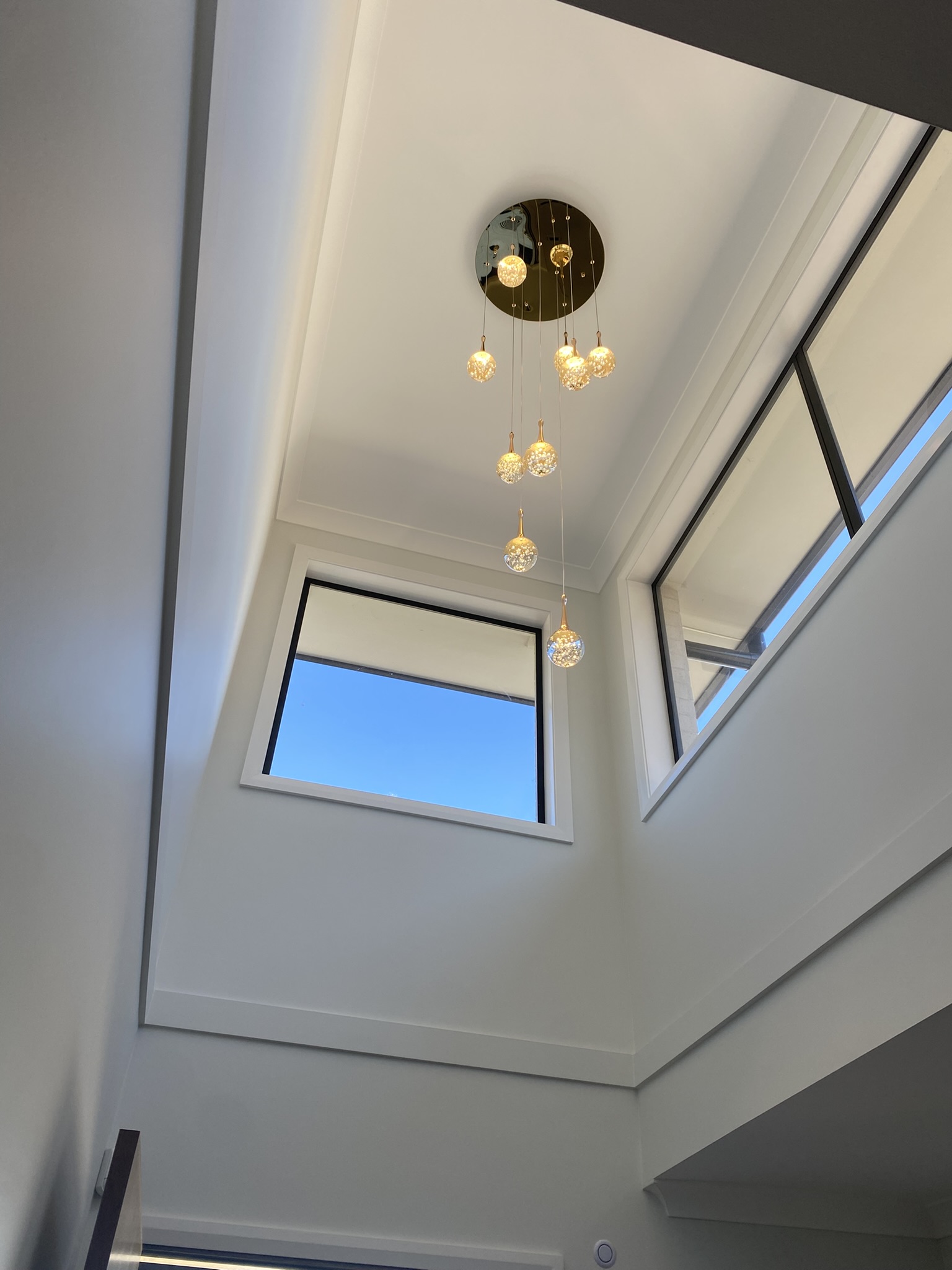 Brass cascading chandelier with crystal orb pendants in a double-height foyer