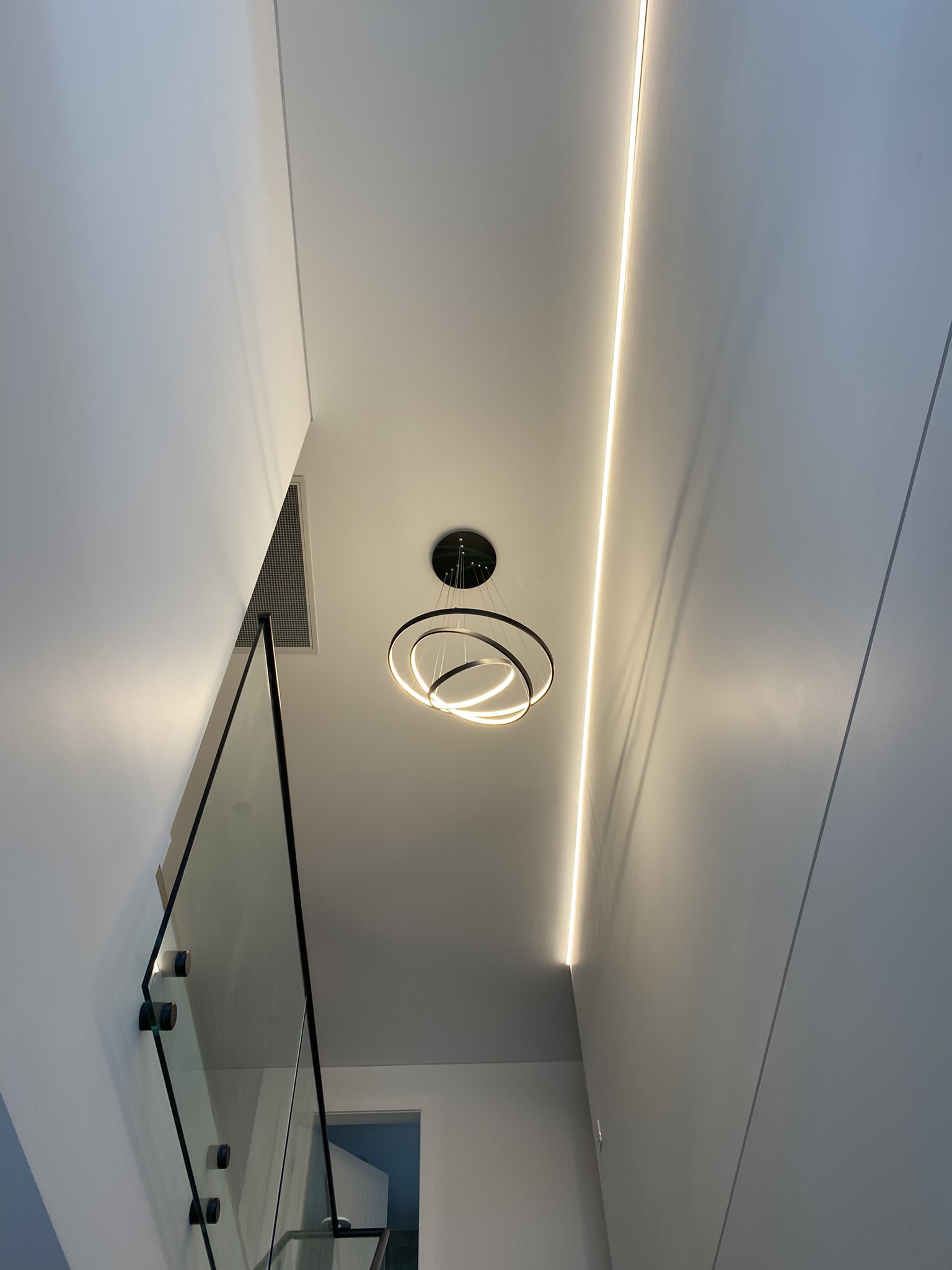 Suspended LED ring chandelier and recessed cove lighting in a stairwell