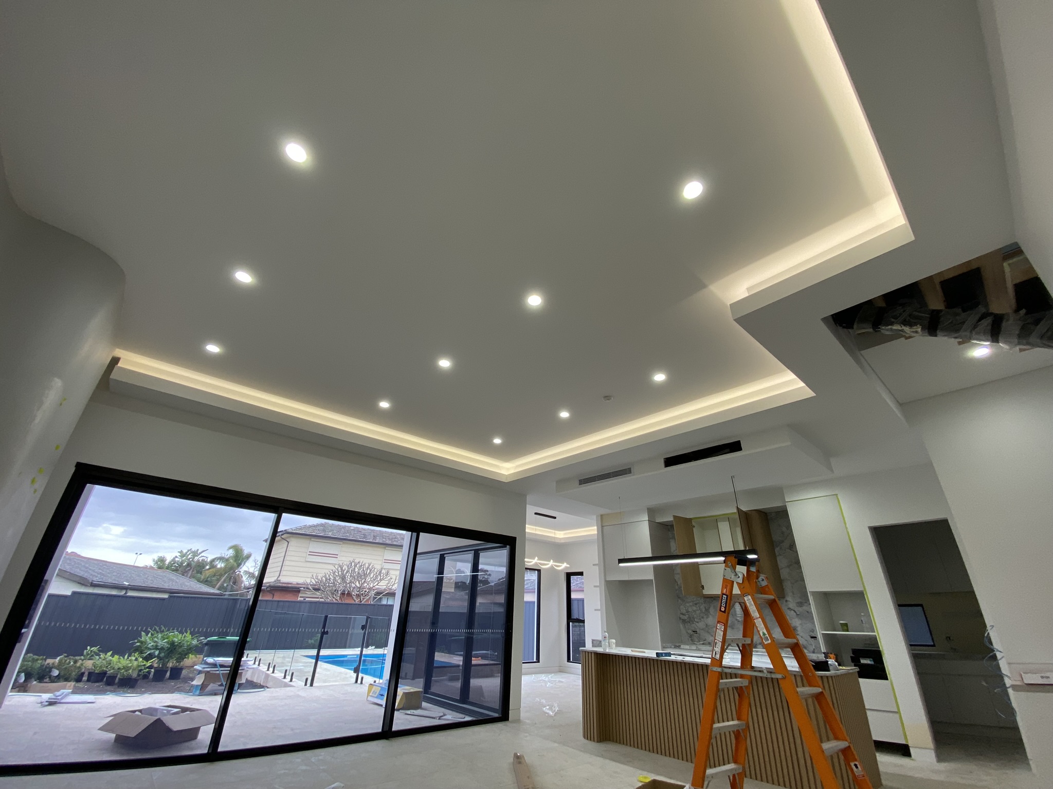 Coffered ceiling with concealed LED cove lighting and recessed downlights over a kitchen and living area