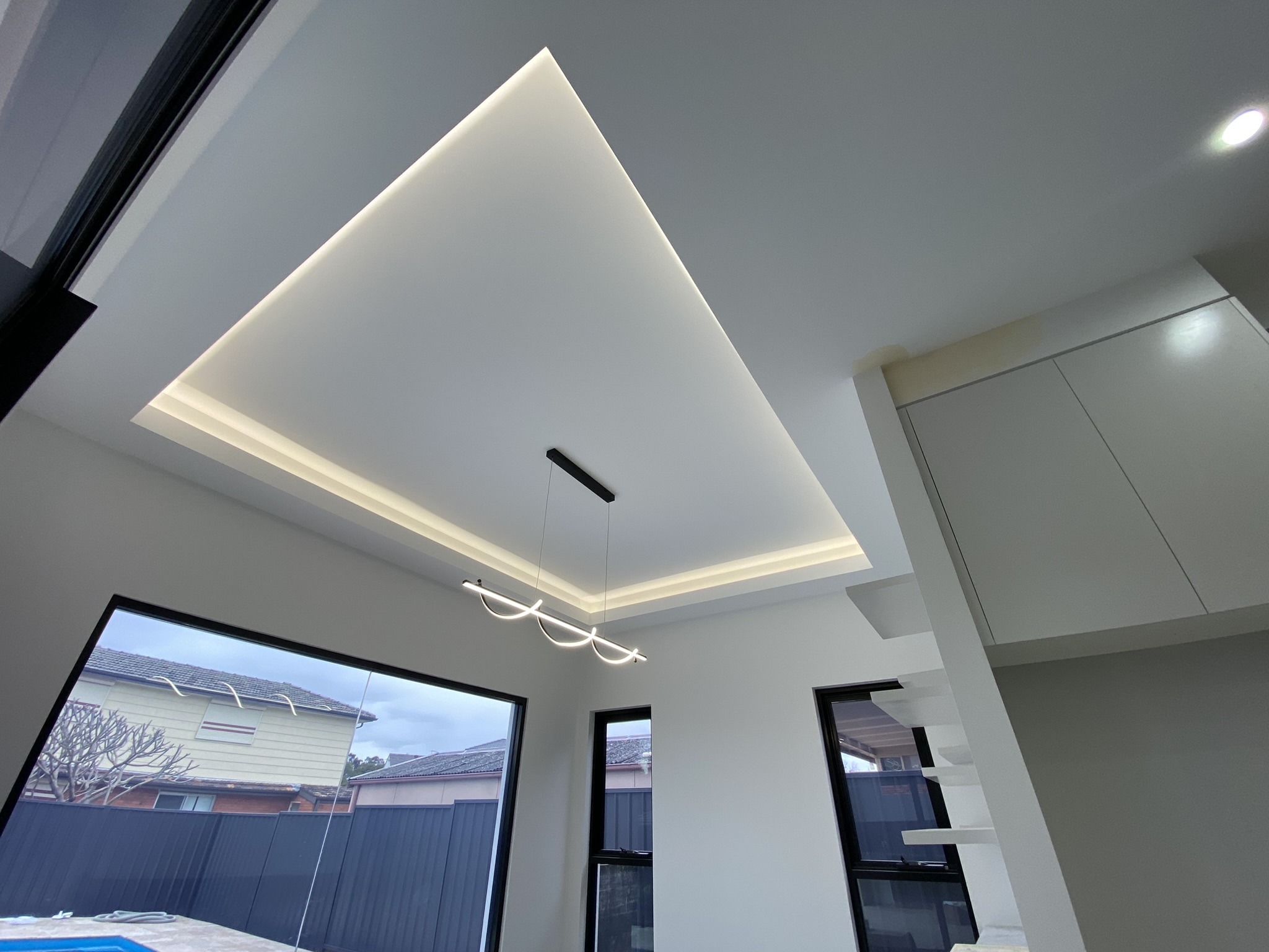 Living and dining area with coffered ceiling cove lighting and a suspended ribbon pendant light