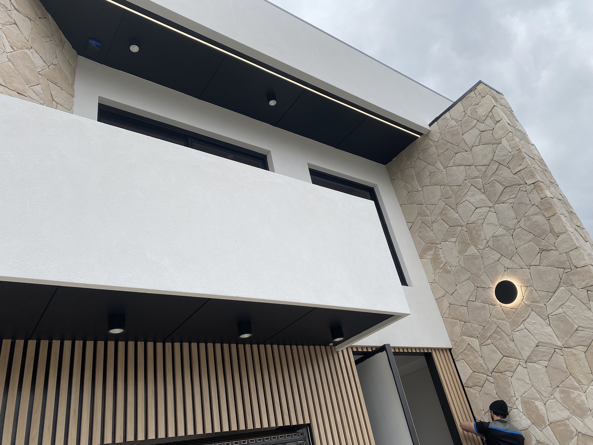 Exterior facade with matte black halo wall sconce and soffit-mounted cylinder downlights