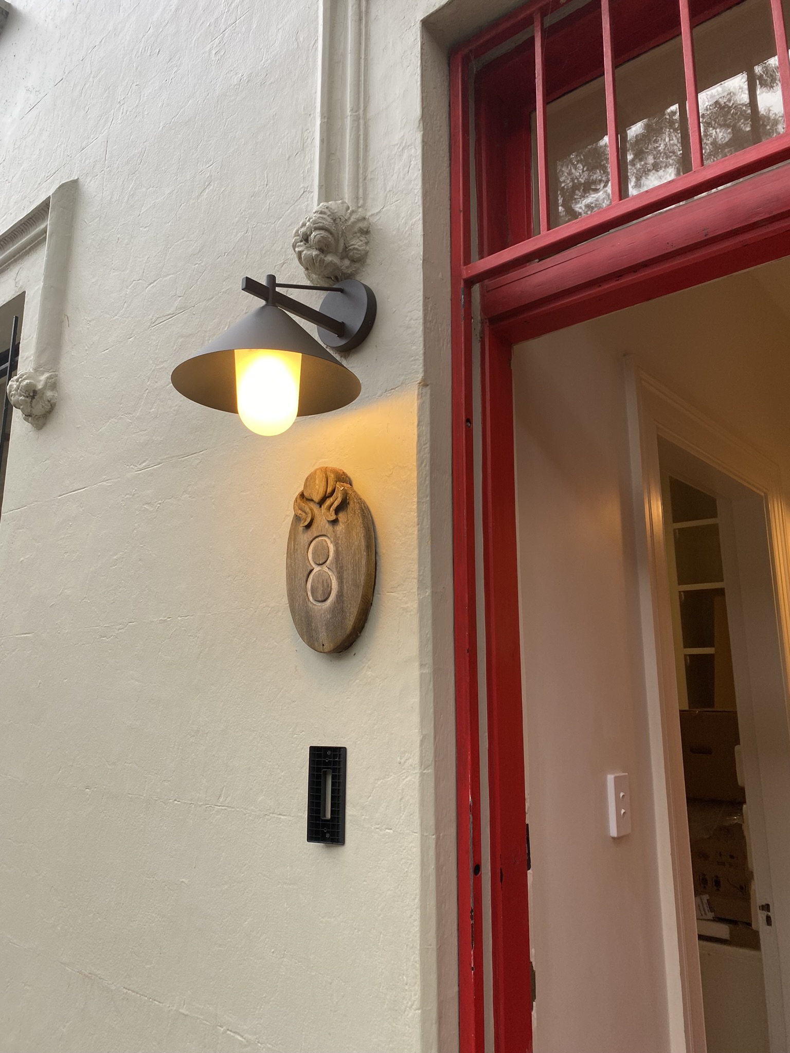 Exterior entrance wall sconce installed above a house number plaque